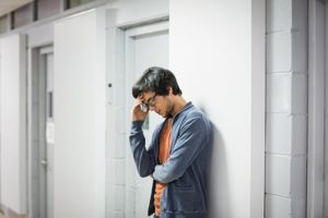 Man holds head in his hands in a hallway pondering frequently asked questions about addiction